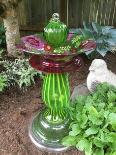 a green glass birdbath sitting on top of a flower pot next to plants