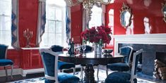 a dining room with red walls, blue chairs and a black table in front of a fireplace