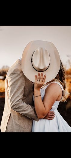 a man in a suit and tie hugging a woman wearing a white dress with a cowboy hat on her head