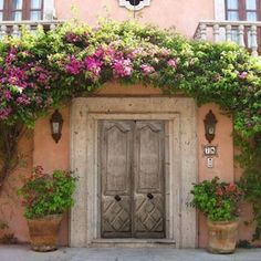 an old building with potted plants and flowers on the outside wall, next to a large wooden door