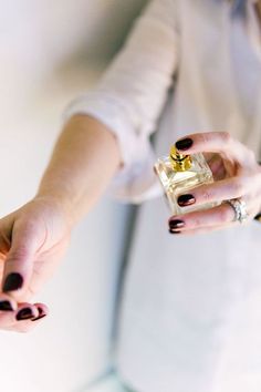 a woman holding a small bottle of perfume in her right hand and wearing black nail polish