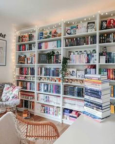 a living room filled with lots of books on top of a white book shelf next to a chair