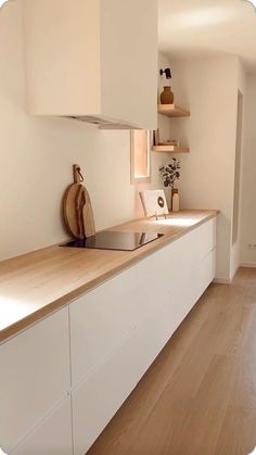 an empty kitchen with white cabinets and wood flooring is seen in this image, there are shelves on the wall