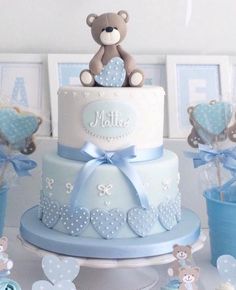 a blue and white baby shower cake with a teddy bear sitting on top of it