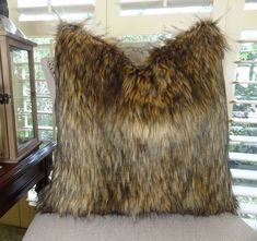 a large furry pillow sitting on top of a white chair in front of a window