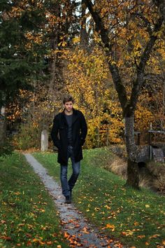 a man is walking down a path in the woods with autumn leaves on the ground