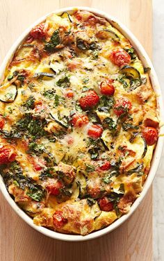 a casserole with tomatoes, spinach and cheese in a white dish on a wooden surface