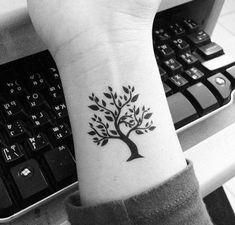 a black and white photo of a tree tattoo on the left wrist, next to a keyboard