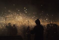 fireworks are lit up in the night sky as people walk by on their cell phones