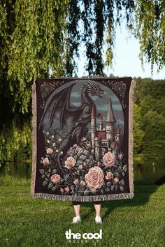 a woman standing in the grass holding up a blanket with a dragon and roses on it