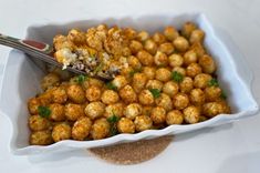 a white dish filled with tater tots and garnished with parsley