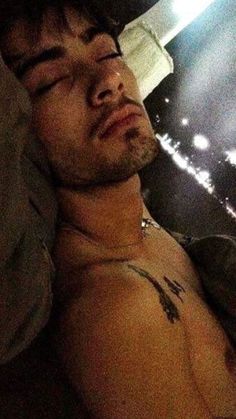 a shirtless man laying on a bed with his eyes closed in the dark at night