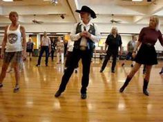 a group of people are dancing in a dance hall with one man wearing a cowboy hat