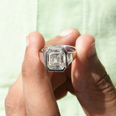 a woman's hand holding a ring with a large diamond in the center, on top of a green towel