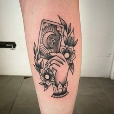 a tattoo on the leg of a person holding a playing card with flowers and leaves