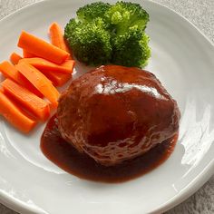 a white plate topped with meat covered in gravy next to carrots and broccoli