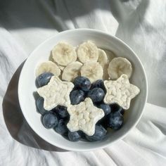 a white bowl filled with blueberries and bananas on top of a white cloth covered table