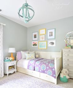 a bedroom decorated in pastel colors with pictures on the wall above the bed and dresser