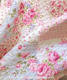 a pink and white flowered quilt is laying on top of a tablecloth that has been folded over