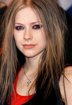 a girl with long hair and blue eyes looks at the camera while wearing a red top