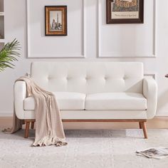 a living room with white furniture and pictures on the wall above it, along with a throw blanket