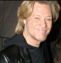 a man with blonde hair wearing a black shirt and smiling at the camera while standing next to a woman