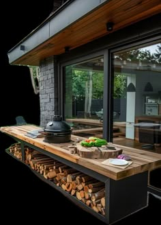 an outdoor kitchen with wood stacked on the counter and grilling area in front of it