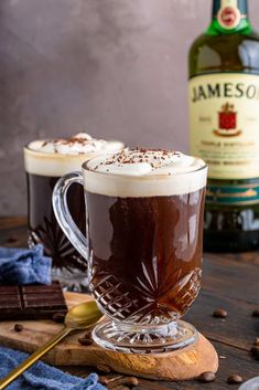 two mugs filled with hot chocolate and topped with marshmallows next to a bottle of jameson