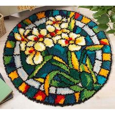 a colorful rug with flowers on it next to a book and potted plant in the background