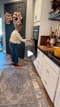 a woman is standing in the middle of a kitchen and reaching into an oven with flowers on her head