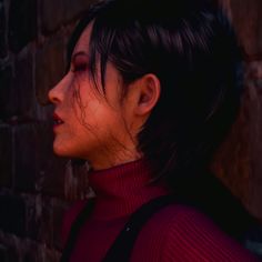 a woman standing next to a brick wall wearing a red turtle neck sweater and black suspenders