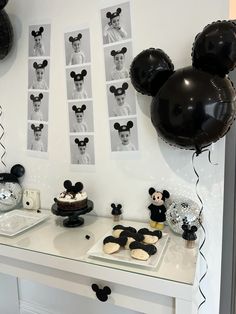 a table topped with balloons and mickey mouse cake next to black and white pictures on the wall