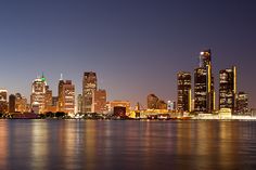 the city skyline is lit up at night, reflecting off the water and lights in the foreground