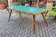 a green table sitting on top of a brick floor next to potted planters