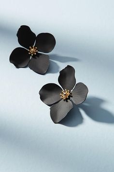 two black flower earrings on a light blue surface with shadows coming from the top and bottom