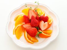 strawberries, oranges and lemon slices on a white plate with green sprigs