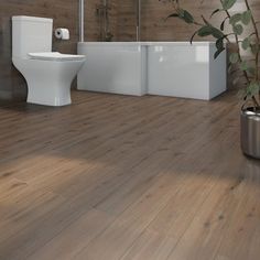 a white toilet sitting next to a plant on top of a wooden floor in a bathroom