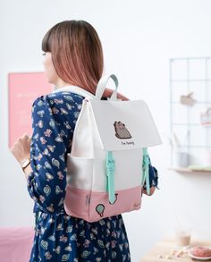 a woman wearing a white and pink backpack with a cat on the front, while standing next to a table