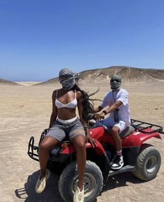 a man and woman riding on the back of a red four - wheeler in the desert