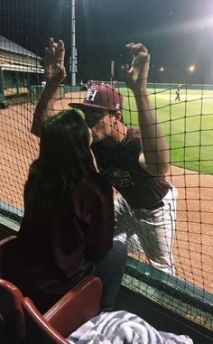 a man and woman sitting in the dugout at a baseball game holding hands up