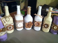 six wine bottles decorated with flowers and burlocks