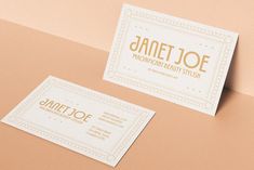 two white business cards with gold foil on them sitting on top of a pink surface