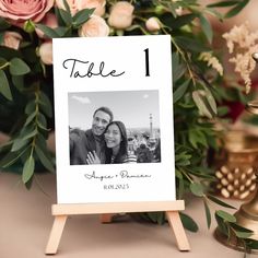 a table number sign sitting on top of a wooden easel next to flowers and candles