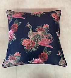 a blue pillow with pink flowers and birds on the front, sitting on a tile floor