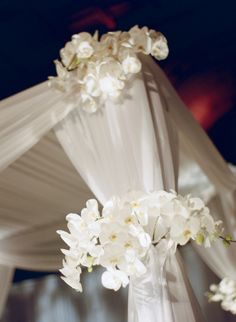 white flowers are placed in a vase on the top of a wedding table with draping