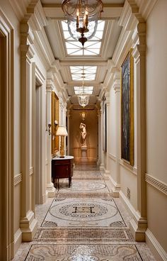 an elegant hallway with chandelier and art work on the walls, along with marble flooring