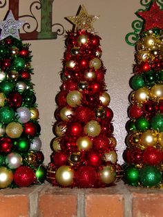 three christmas trees are sitting on top of a brick wall and one is decorated with ornaments