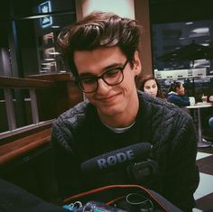 a young man wearing glasses sitting in front of a microphone and smiling at the camera