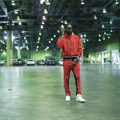 a man standing in an empty parking garage talking on his cell phone while wearing red sweat suit and white sneakers