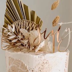 a wedding cake decorated with gold leaves and the word love spelled in cursive writing